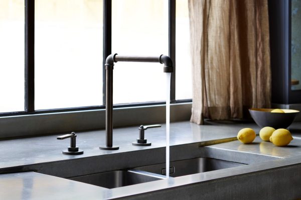 Concrete kitchen worktop with blackened bronze tap beside steel framed window