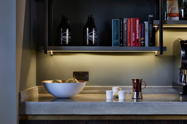 Dark oak kitchen cabinetry with illuminated shelving and concrete worktop